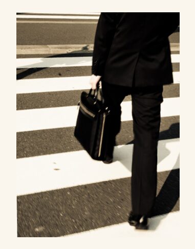 A person in black suit and briefcase crossing the street.